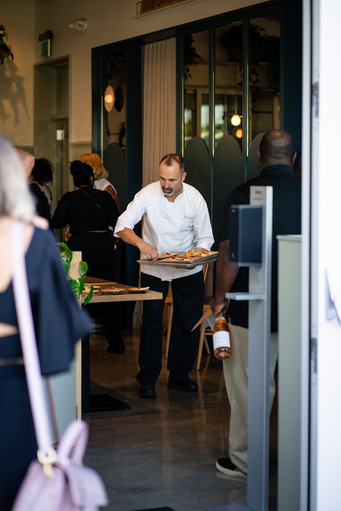 A waiter stands and serves food on a tray to customers in a bustling restaurant setting.